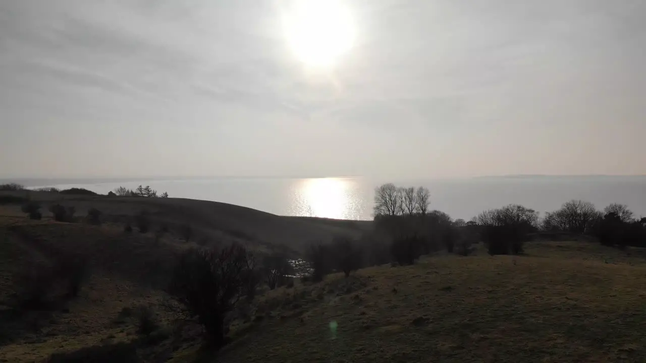 Aerial view of beautiful green hills moving toward the sunset above the blue sea in Sejerøbugten Denmark