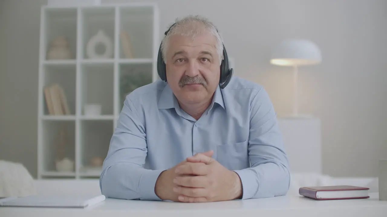 middle-aged man with headphones on head is nodding and looking at camera video calling and online chatting concept