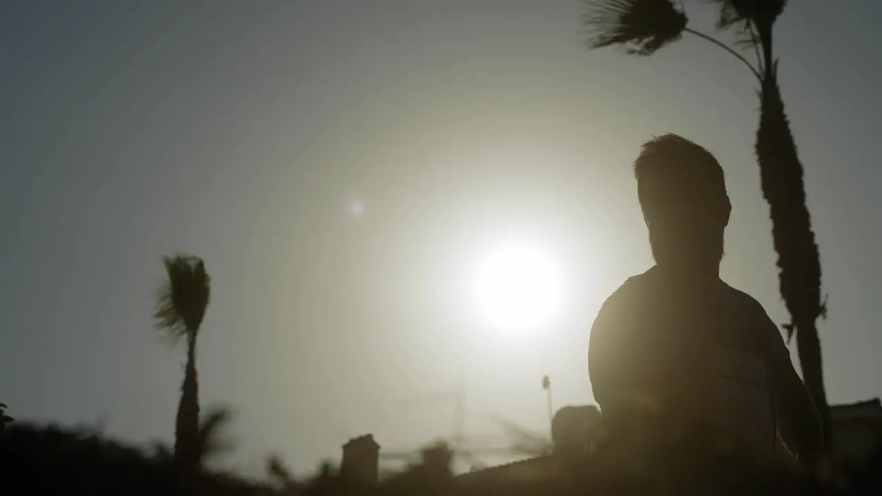 A man raking his garden silhouetted against a bright sunny sky