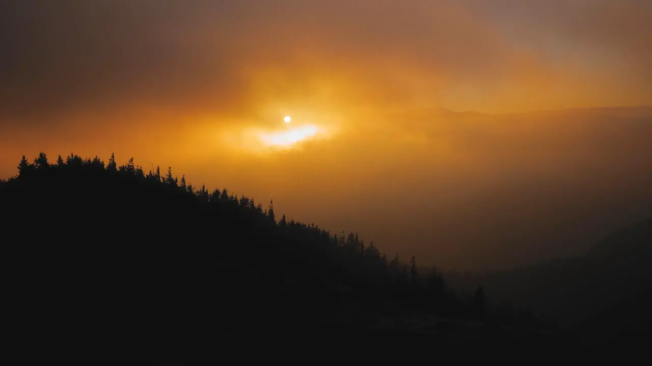 A shoot of an epic surreal orange sunset over a mountain covered with pine trees