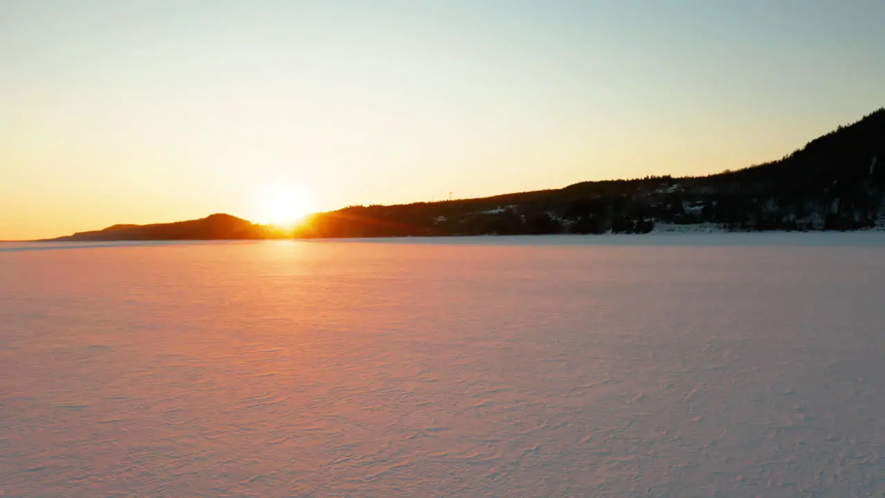 Low aerial flying across a snow covered river as the sun goes down