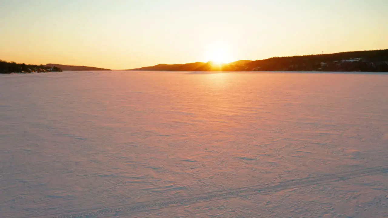 Picturesque aerial flying across a snow covered river as the sun sets along the horizon