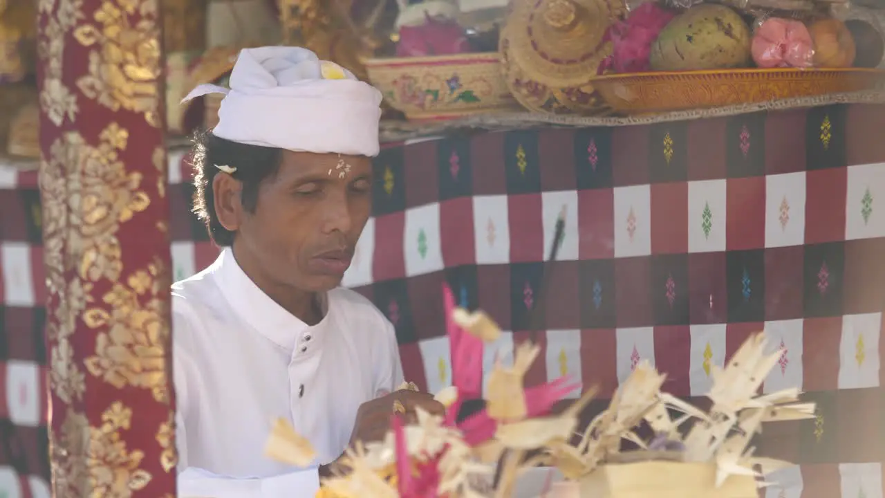 Hindu priest praying at a colorfully decorated altar with flower offering flicks away flower petal when prayer is finished