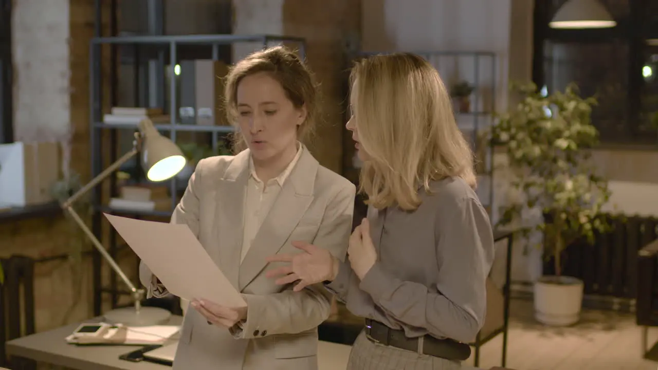 Two Female Coworkers Talking And Reading A Document Standing In The Office