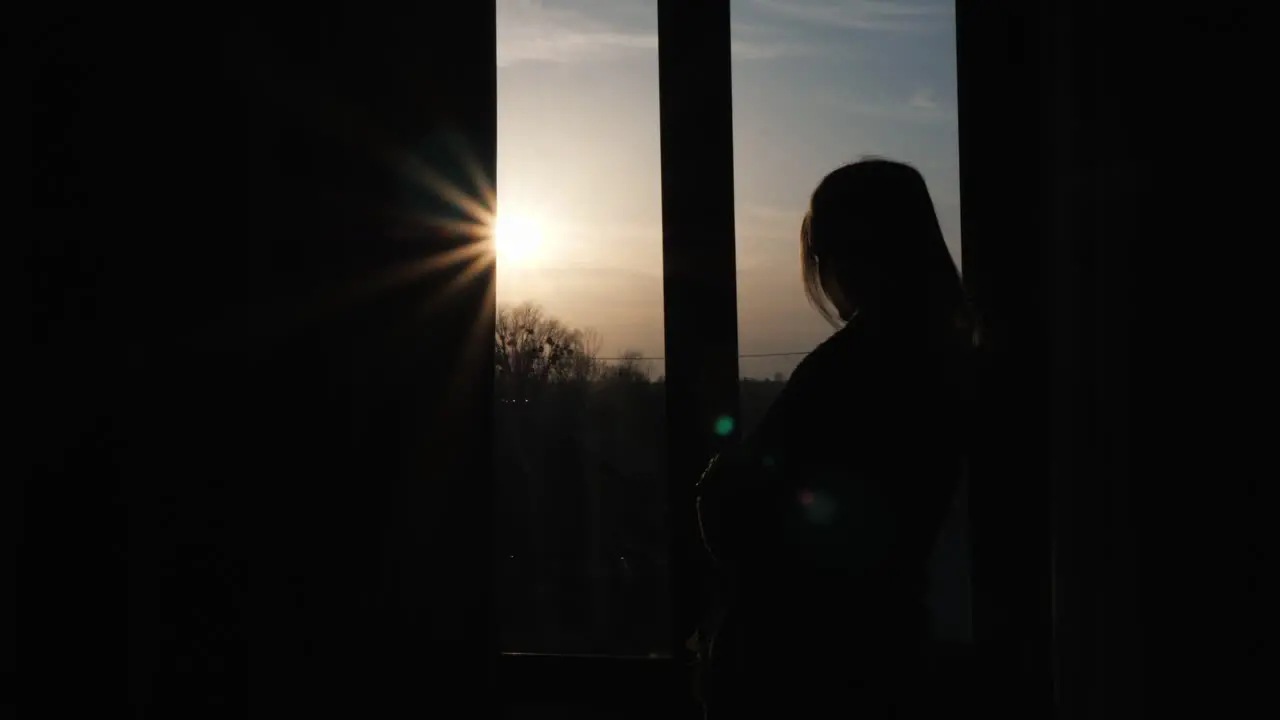 The silhouette of a lonely woman sitting on the window sill and looking out the window