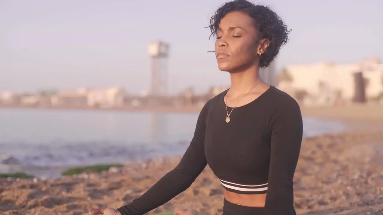 Black afro American woman practicing Vipassana Buddhism meditation in crosslegged position spreading love and positive vibes in the sandy beach of Barcelona Spain at sunrise