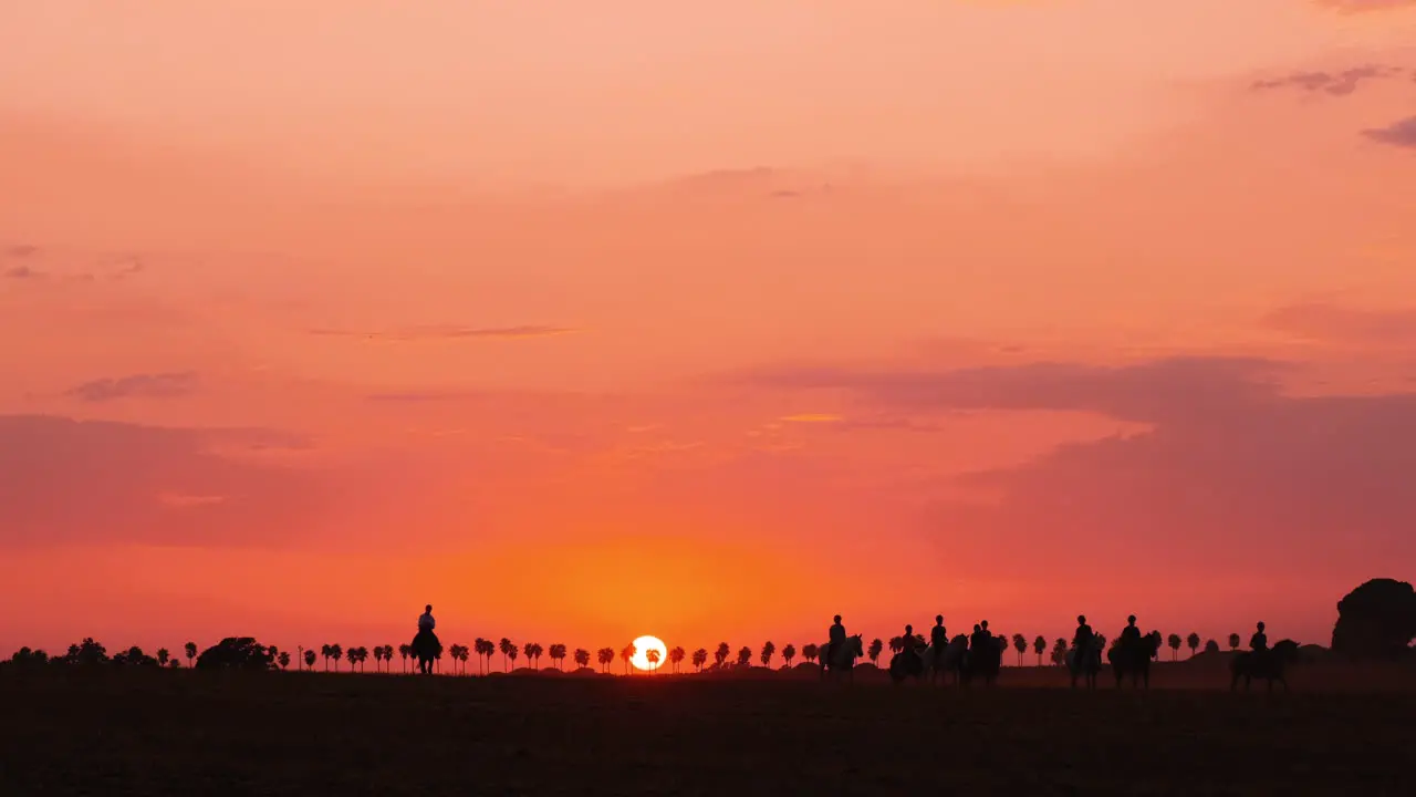 Silhouette of several people riding horses during beautiful orange colored sunset in background