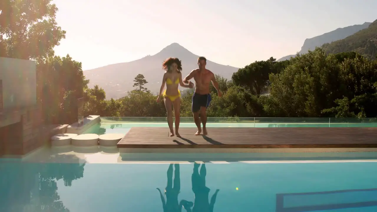 Happy couple leaping into the outdoor swimming pool