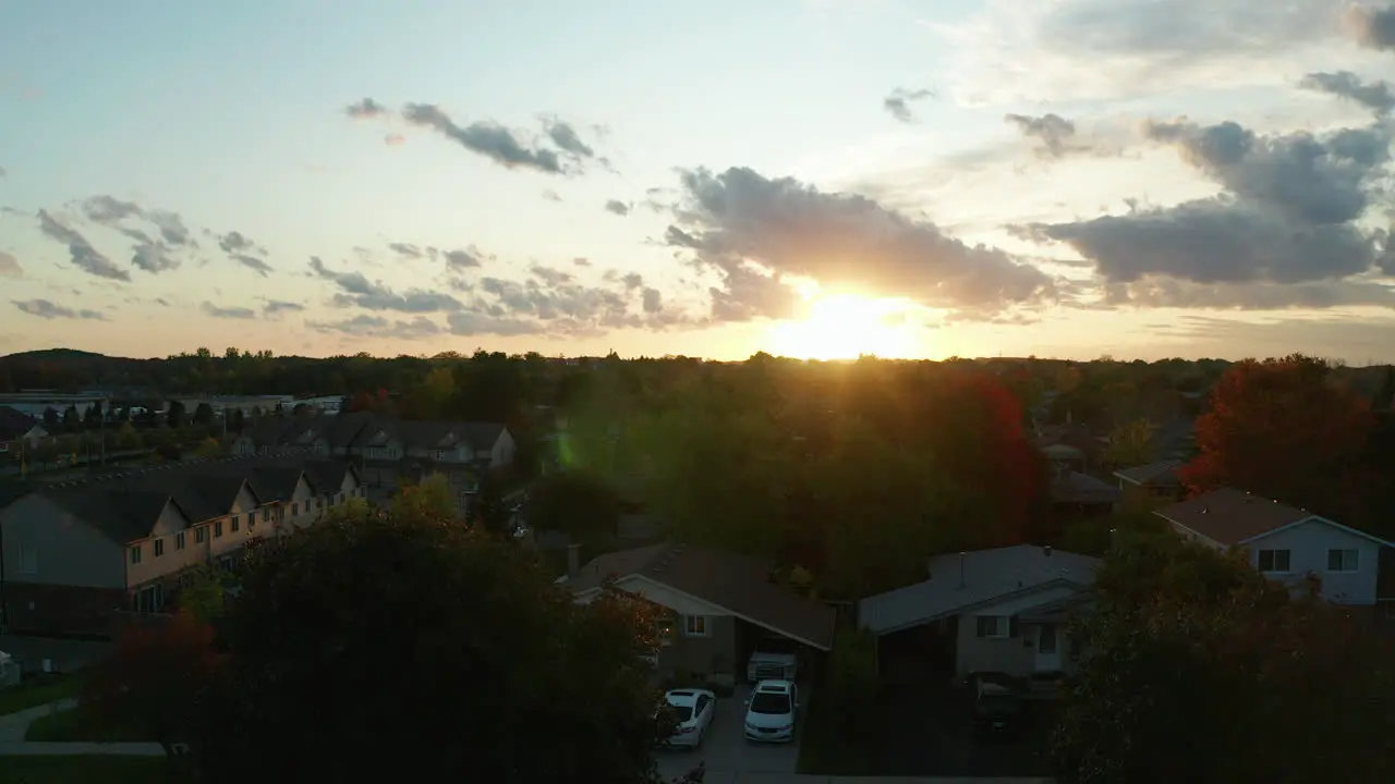 Aerial view ascending over the suburbs at golden hour with the sun in the distance setting and creating a beautiful lens flare