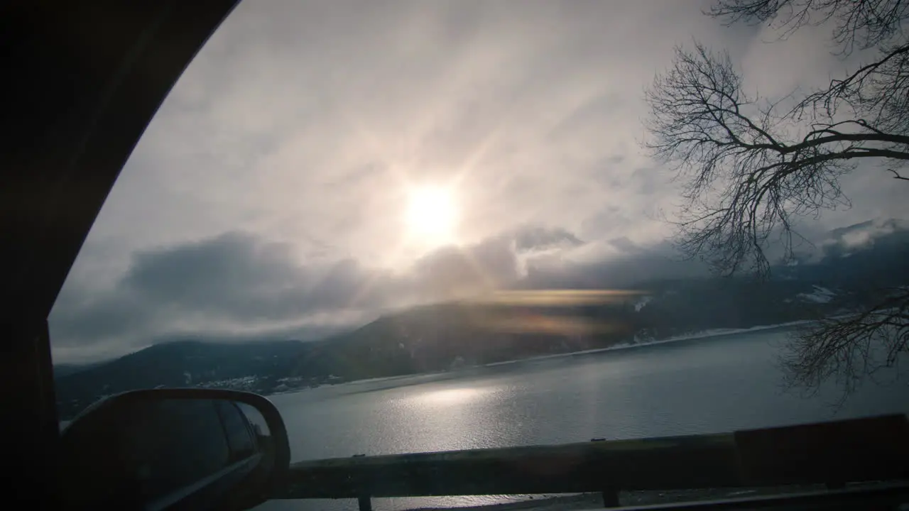 View from car side window on lake and mountains backlit by sun slow motion drive