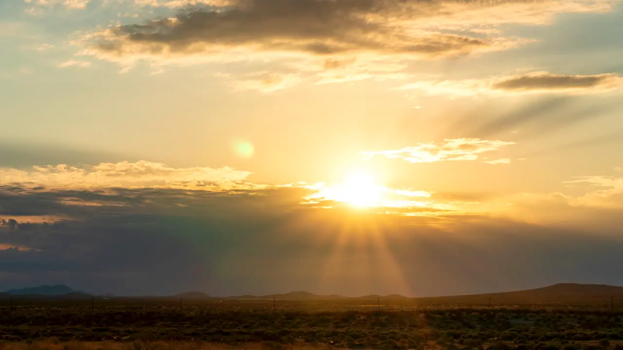 Rays of sun pierce the clouds as the sunrise lights the Mojave Desert landscape static time lapse