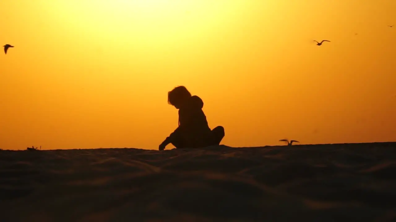 Girl sitting in lotos position at sunrise beach and birds flying away