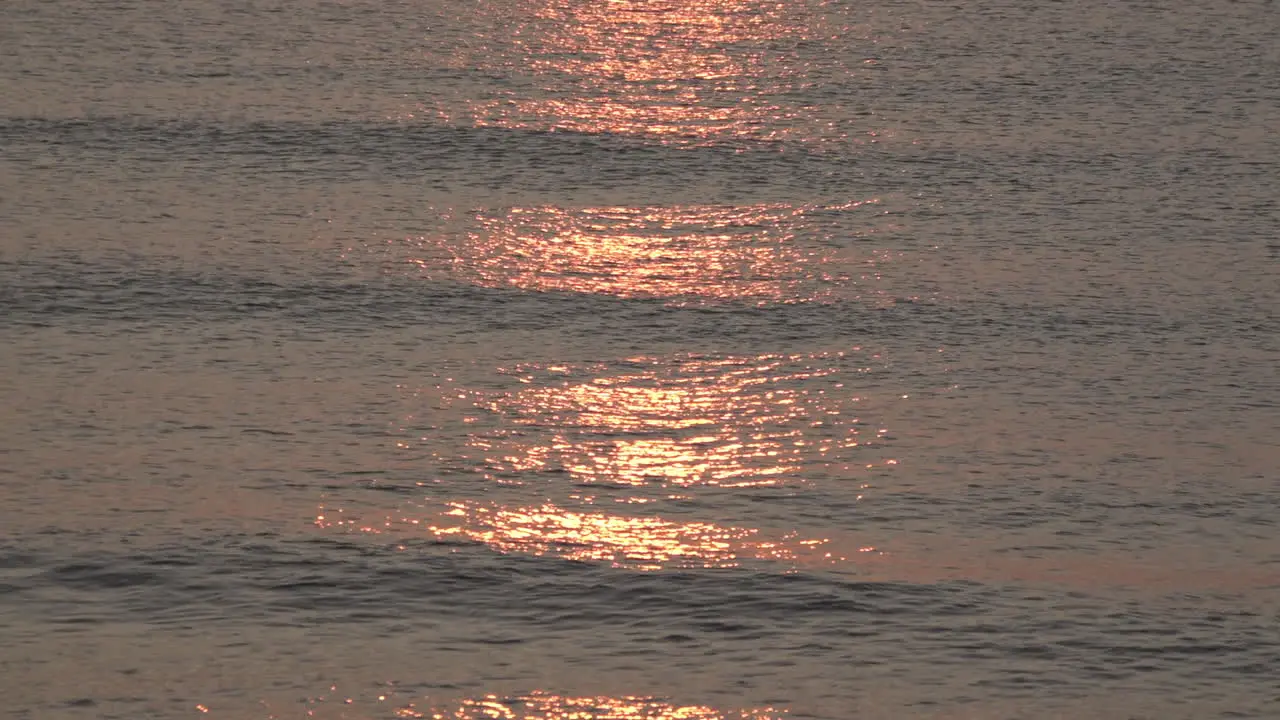 A slow motion shot of a stunning red and golden sunrise reflects on calm silvery waters as small waves roll in