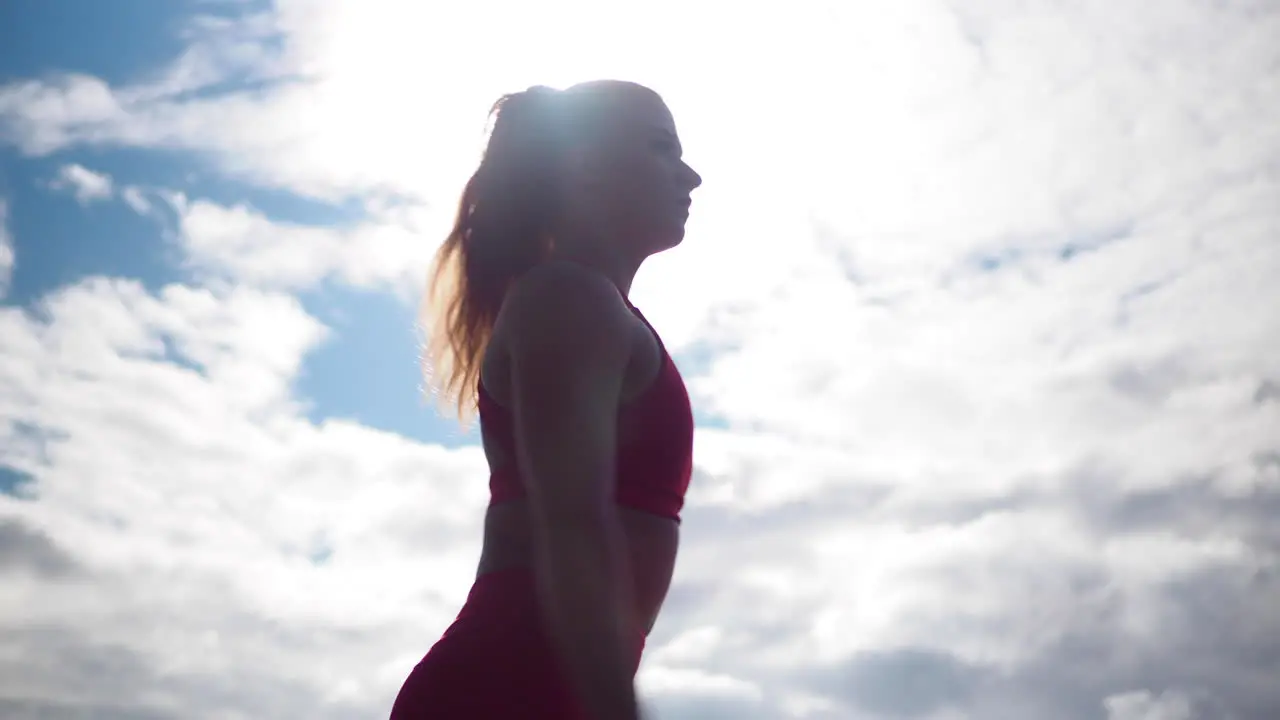 Young woman in red sportswear doing exercises and practicing yoga outside