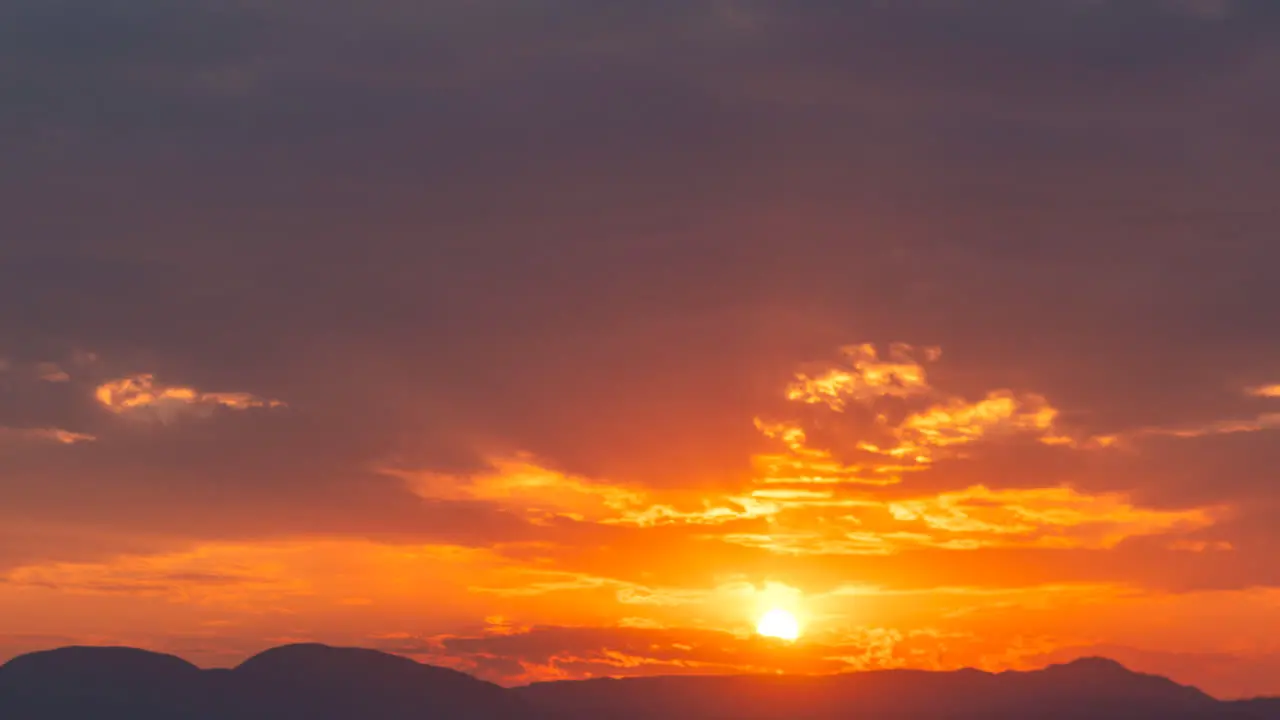 A stunning and colorful sunset beyond the Mojave Desert mountains with golden rays filtering through the cloudscape static time lapse