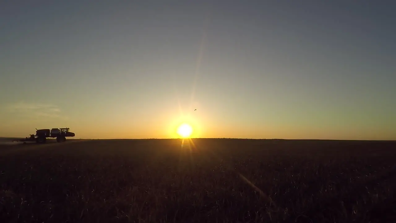 Silhouette Of A Moving Agricultural Tractor Spraying Herbicide At Farmland During Golden Hour