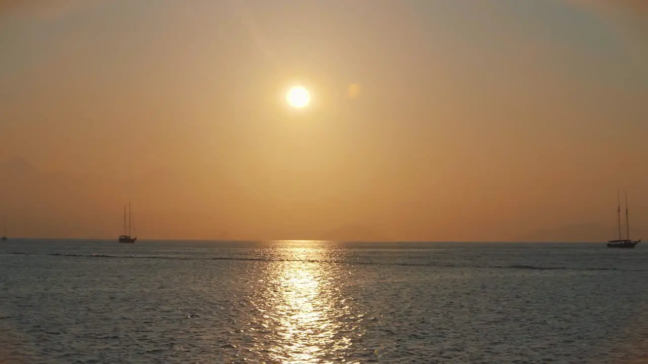 Beautiful and calm golden hour sunset over Mediterranean sea with few sailing boats in distance while sailing on ship in Turkey