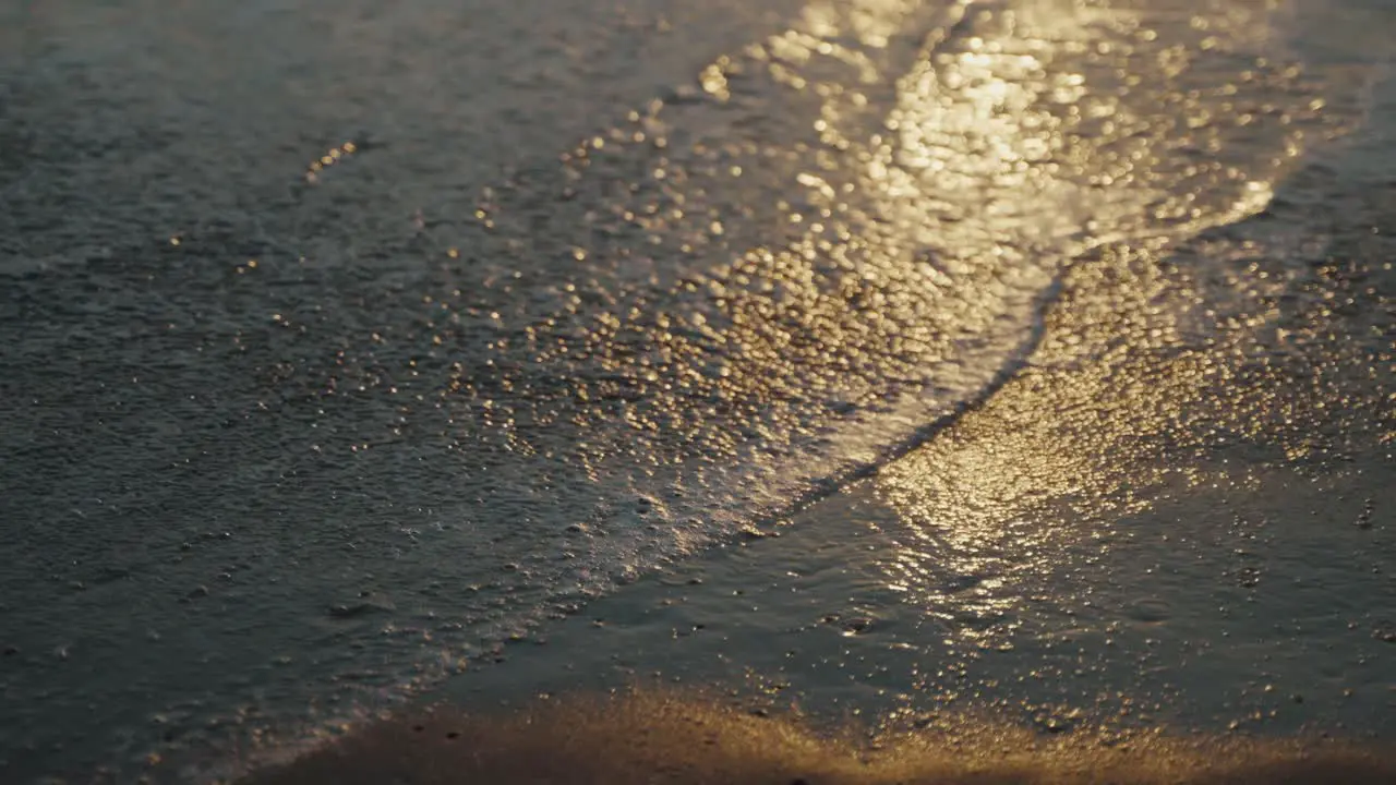 Water receding after a big wave over a sandy beach in Mexico as the light of the setting sun sparkles in the water