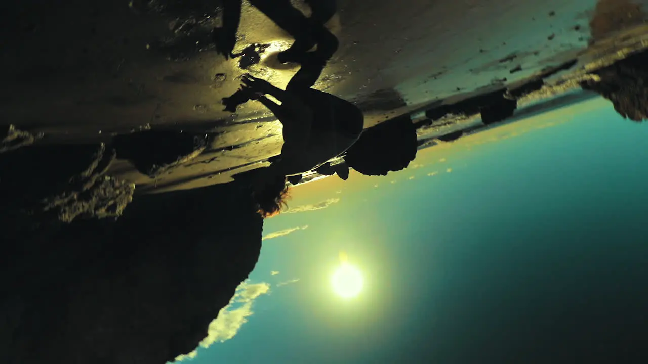 Athletic man does a backflip on the shore of the beach silhouetted in front of the bright sun light