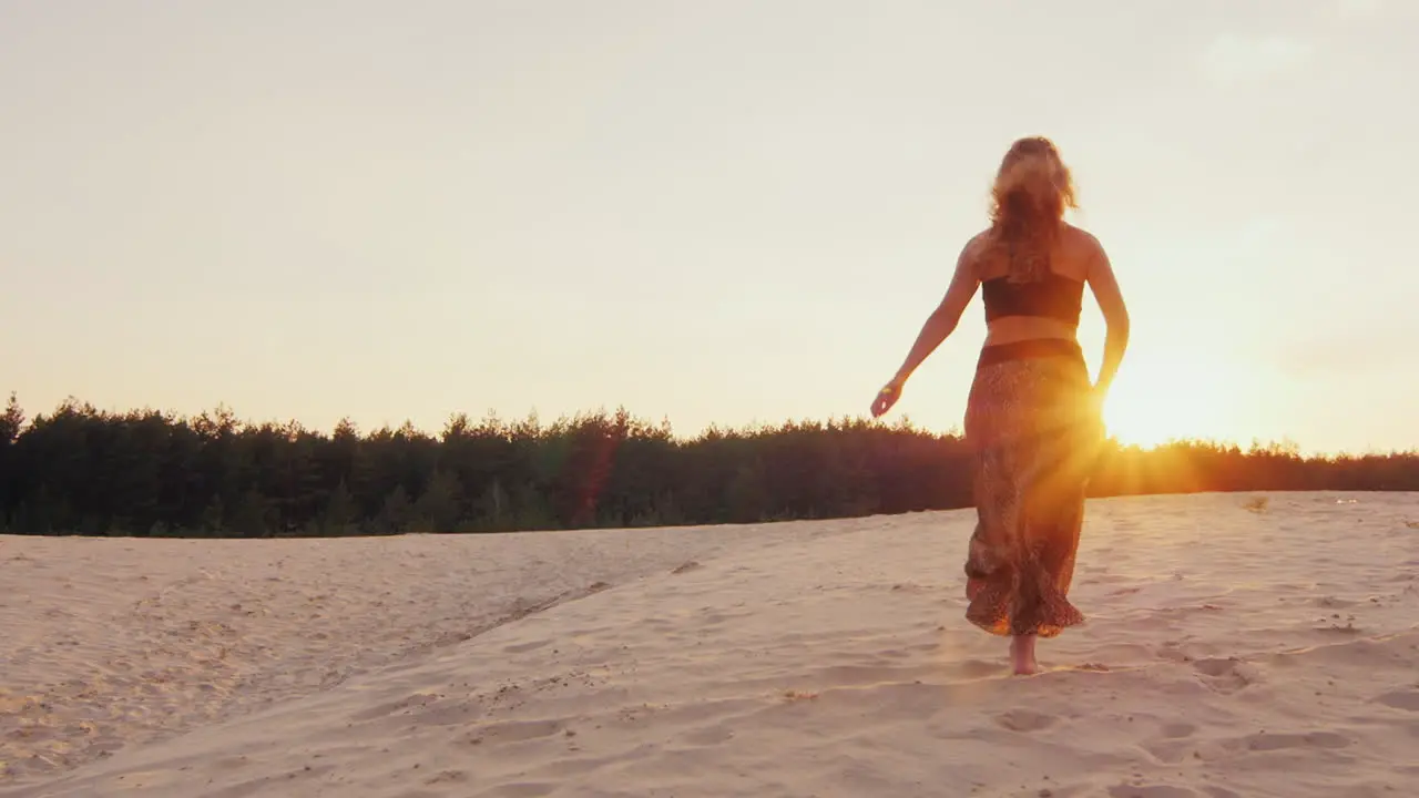 Young Woman In A Beautiful Dress Light Runs Along The Beach Into The Sunset Stretching His Arms To T