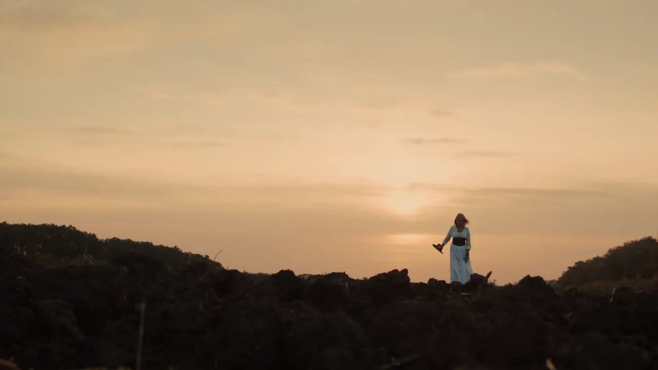 A woman in a dress walks through a plowed field on black soil 1