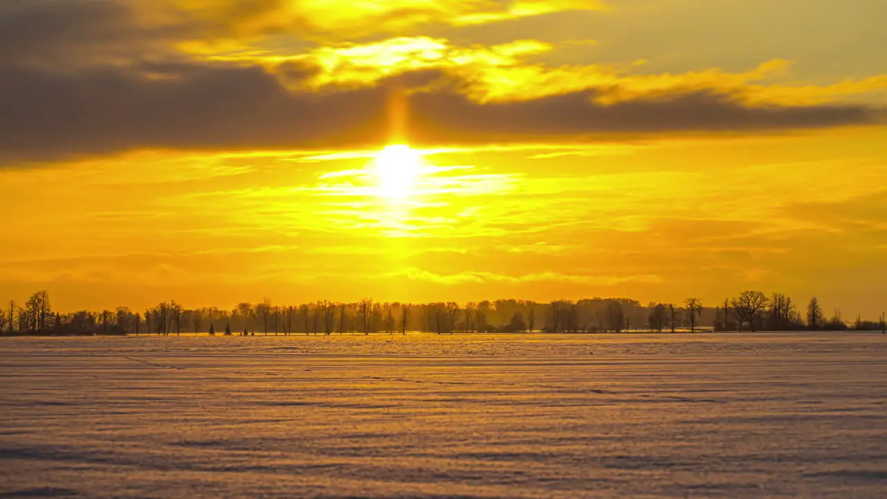 time lapse of fairytale winter landscape with a snowy meadow and trees under a yellow and orange sun