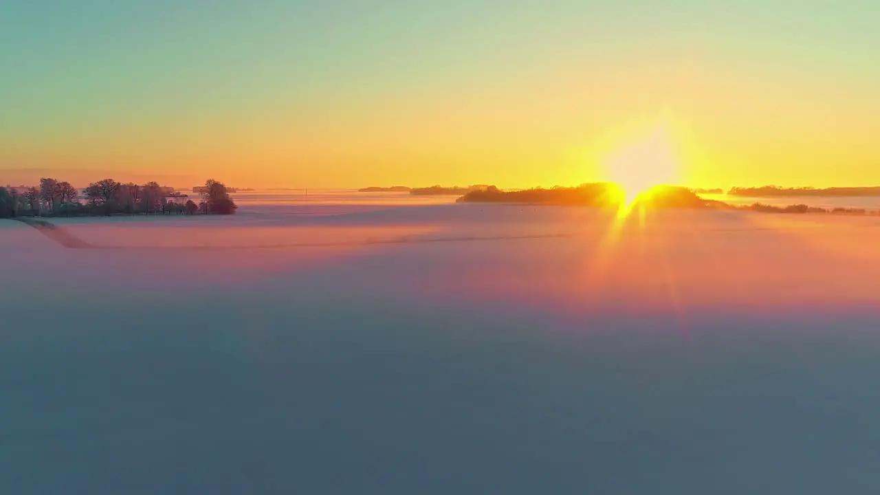 The sun sets on the horizon and glows on the snowy fields of a winter landscape aerial view