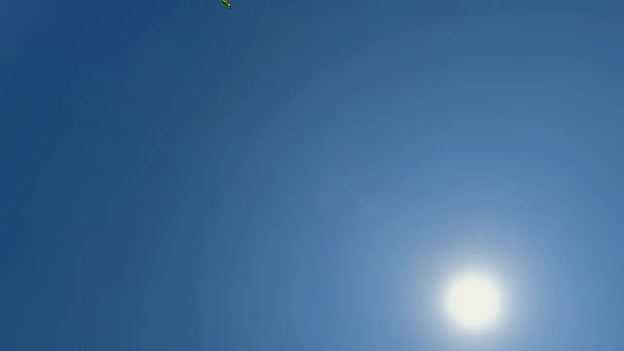 Unusual perspective of flying green toy kite close to shining sun in clear blue sky