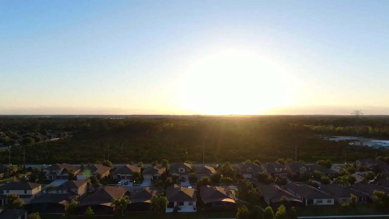 Pan with a lens flare across homes and an orange tree farm during a beautiful sunset