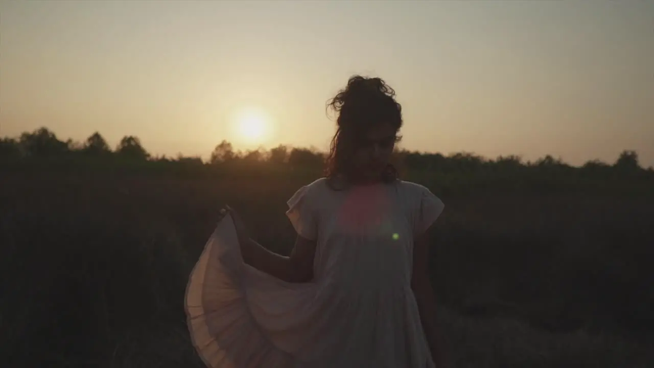 Slow motion static shot of a young pretty indian woman standing on a field in nature during a beautiful sunset