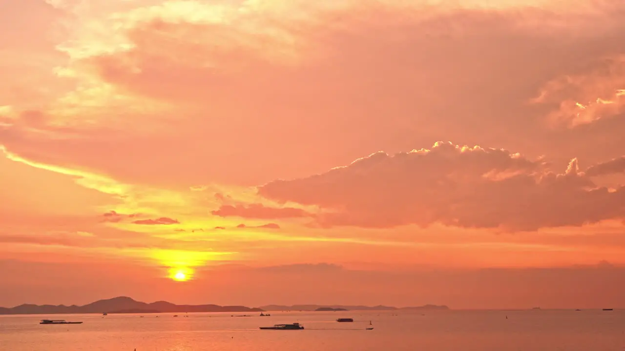 locked wide shot of a beautiful orange golden sunset above the ocean in Thailand with small fisher boats and mountains on the horizon