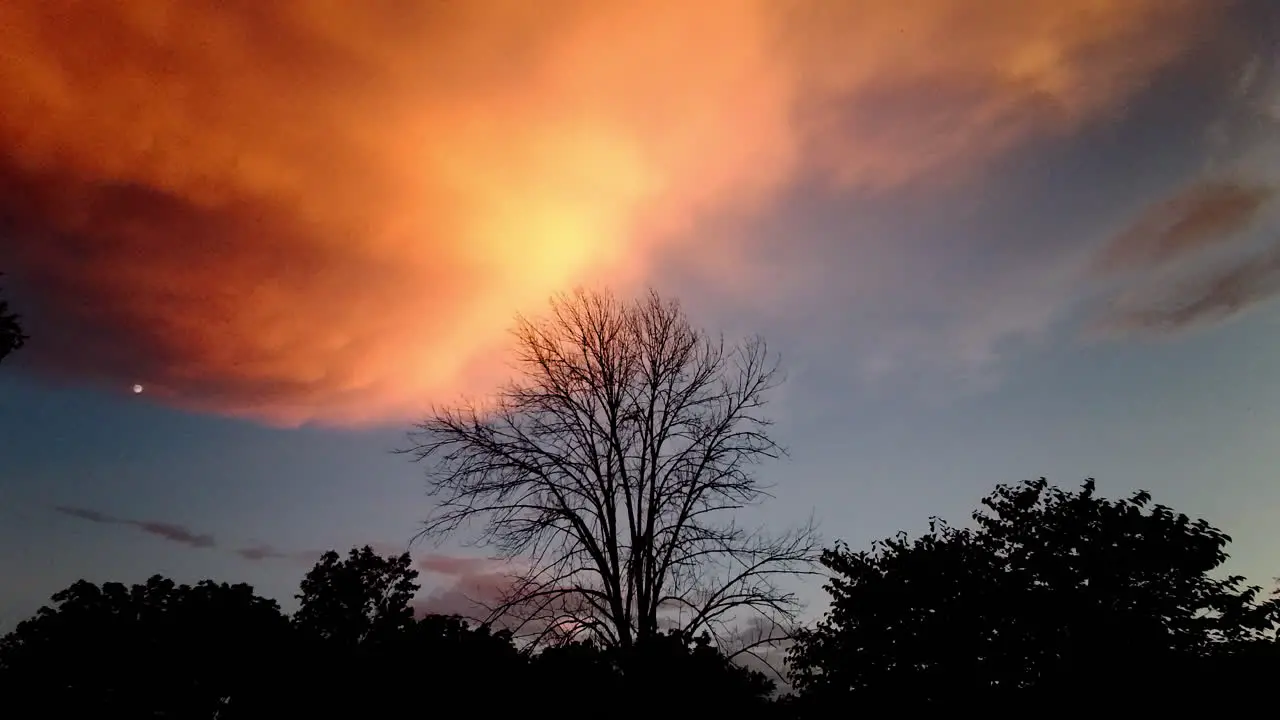 Dramatic storm clouds at sunset with silhouetted trees and moon