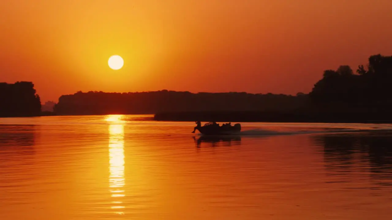 Silhouettes of people in a motor boat sailing along the river at sunset