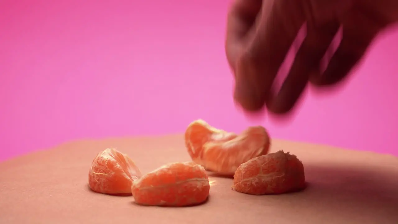 Hand puts ripe peeled mandarins on rotate pink and old paper background 4k video with color correction