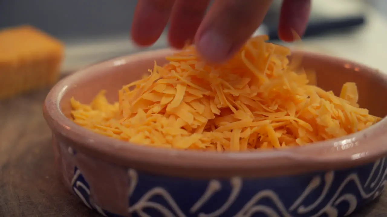 Chef hand mixing a freshly grated pile of cheddar cheese