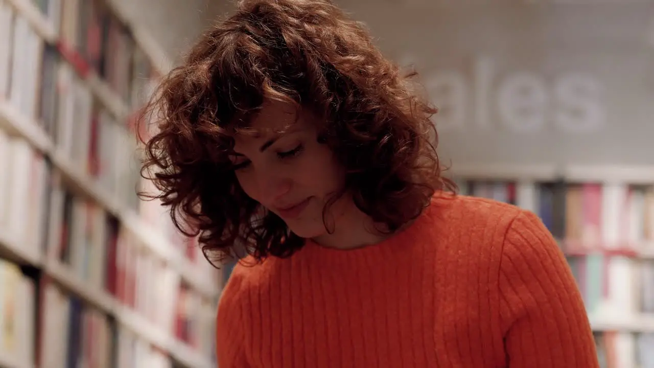 Focused Caucasian Curly Woman Studying Among Book Shelves In Library