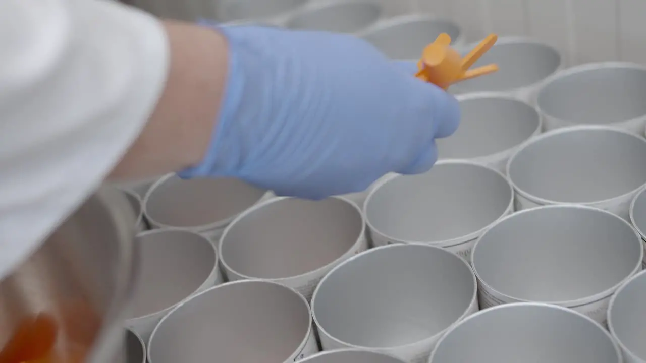 Worker puts small spoons into different cans in a modern clean factory