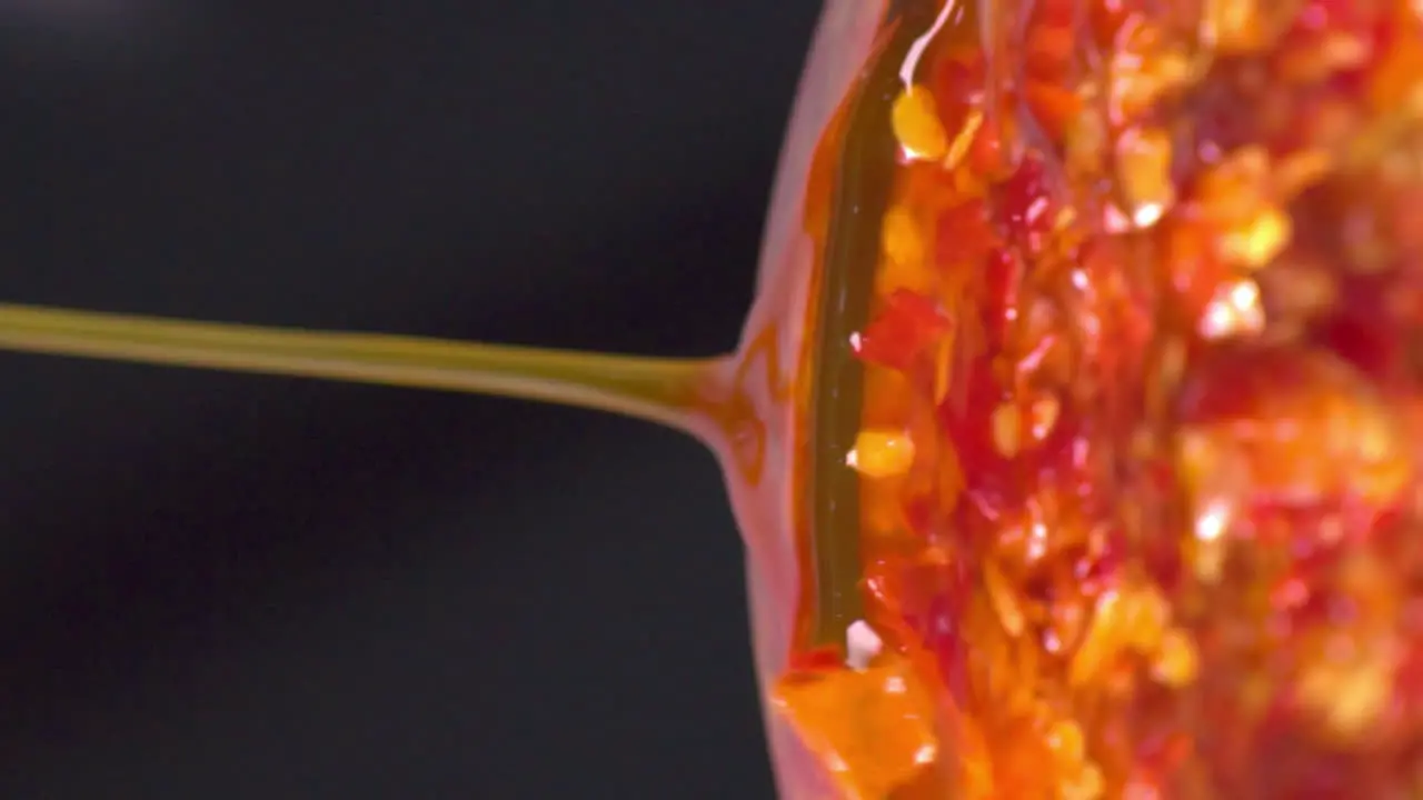 Antigravity horizontal perspective of isolated colorful traditional authentic sambal oily chili paste dripping pouring down from clear glass bowl black background extreme close up static