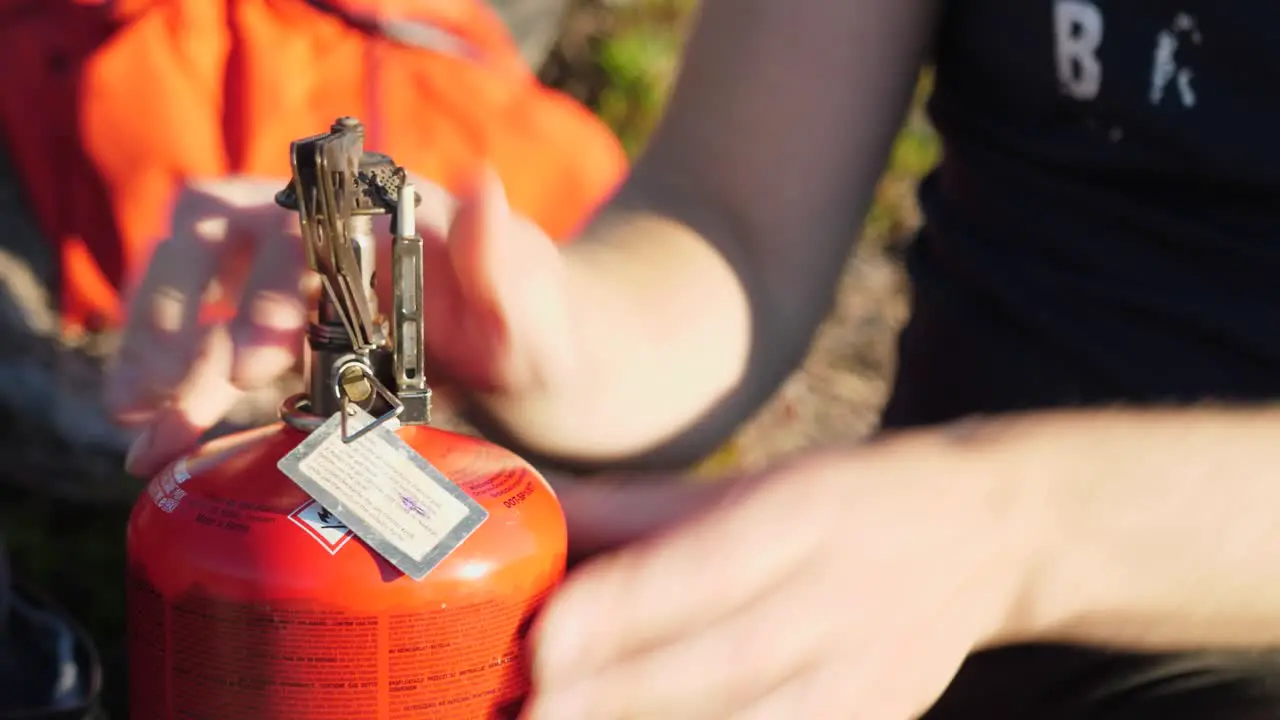 Close up profile shot of person opening metal pan holder on a orange propane camping fuel heater outdoors in a camping environment