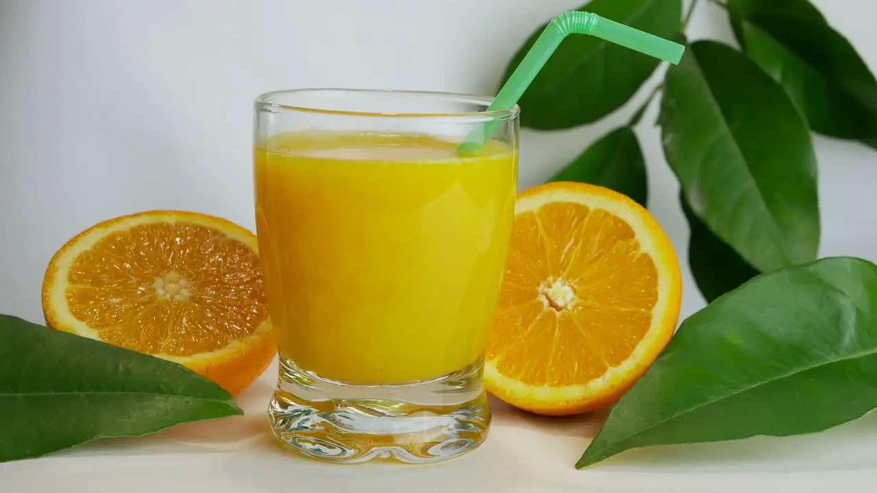 Studio shot of full glass of orange juice and orange halves closeup slow pan