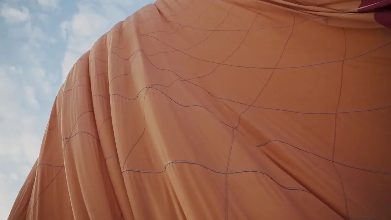 Orange color hot air balloon deflating on ground against blue sky handheld view