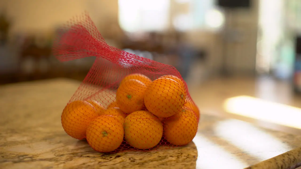 Tripod shot of a man dropping a bag of oranges on a kitchen counter on a warm sunny day