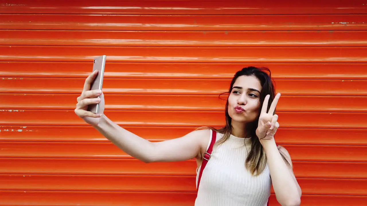 Beautiful young girl takes selfie with smartphone in front of orange red background