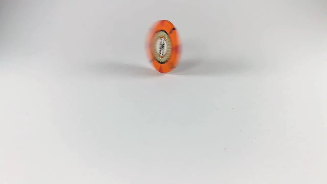 An orange poker chip spinning on a white table STILL ISOLATED SLOMO