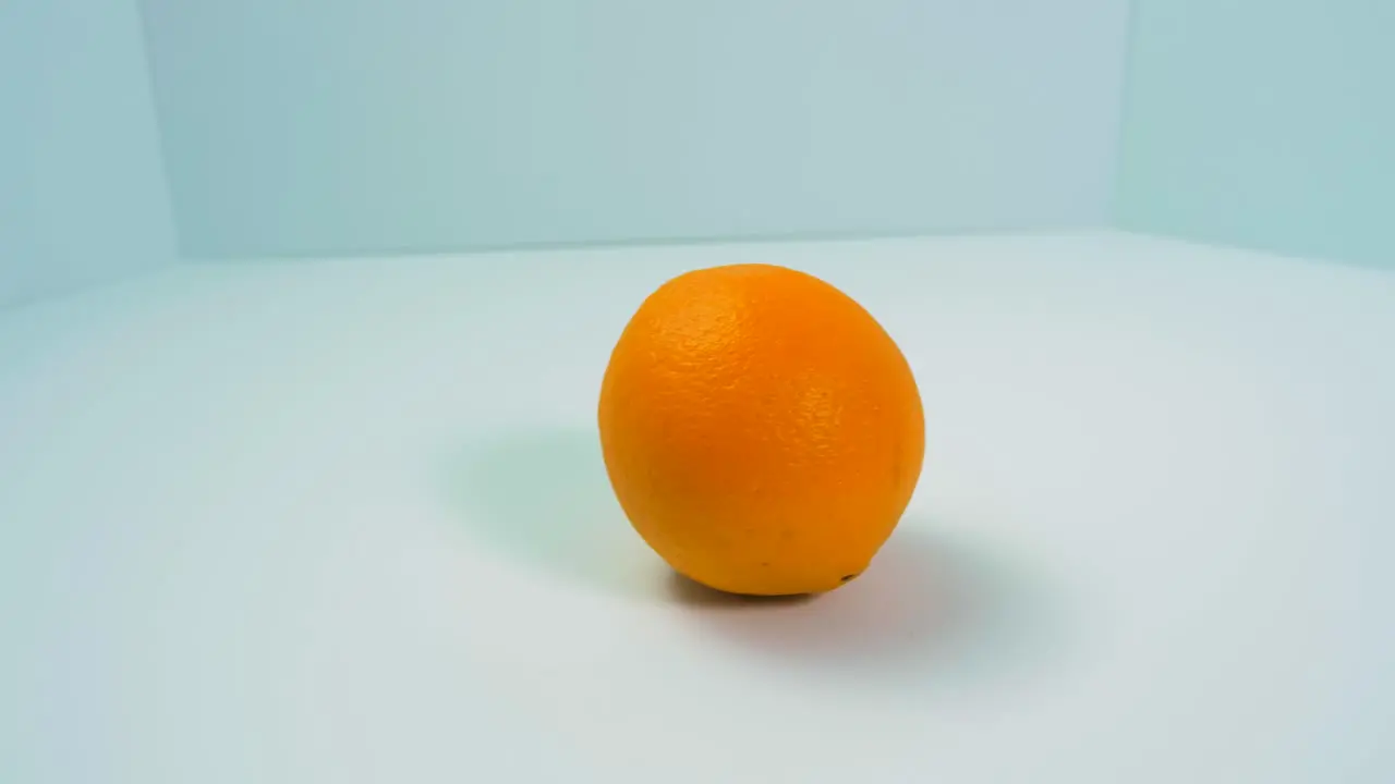 Fresh big juicy orange rotates slowly on a light blue background healthy food concept close up shot camera rotate left