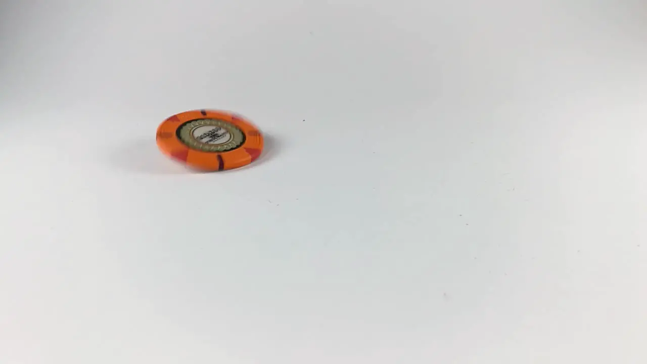 An orange poker chip spinning on a white table STILL ISOLATED