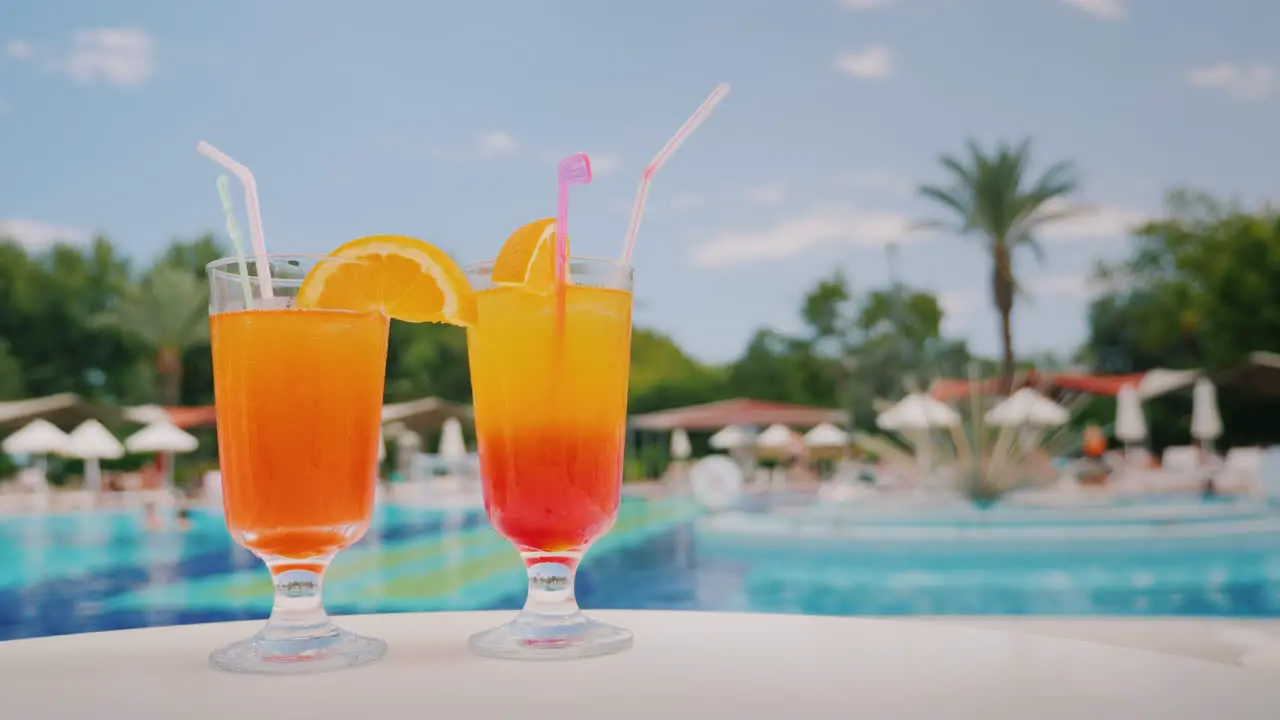 Two Cool Cocktails Stand On The Table On The Background Of The Pool And Palm Trees Paradise And Luxu