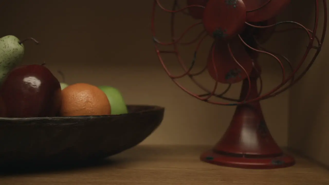 Sliding shot of vintage retro fan and a bowl of fruit pears oranges apples on a shelf