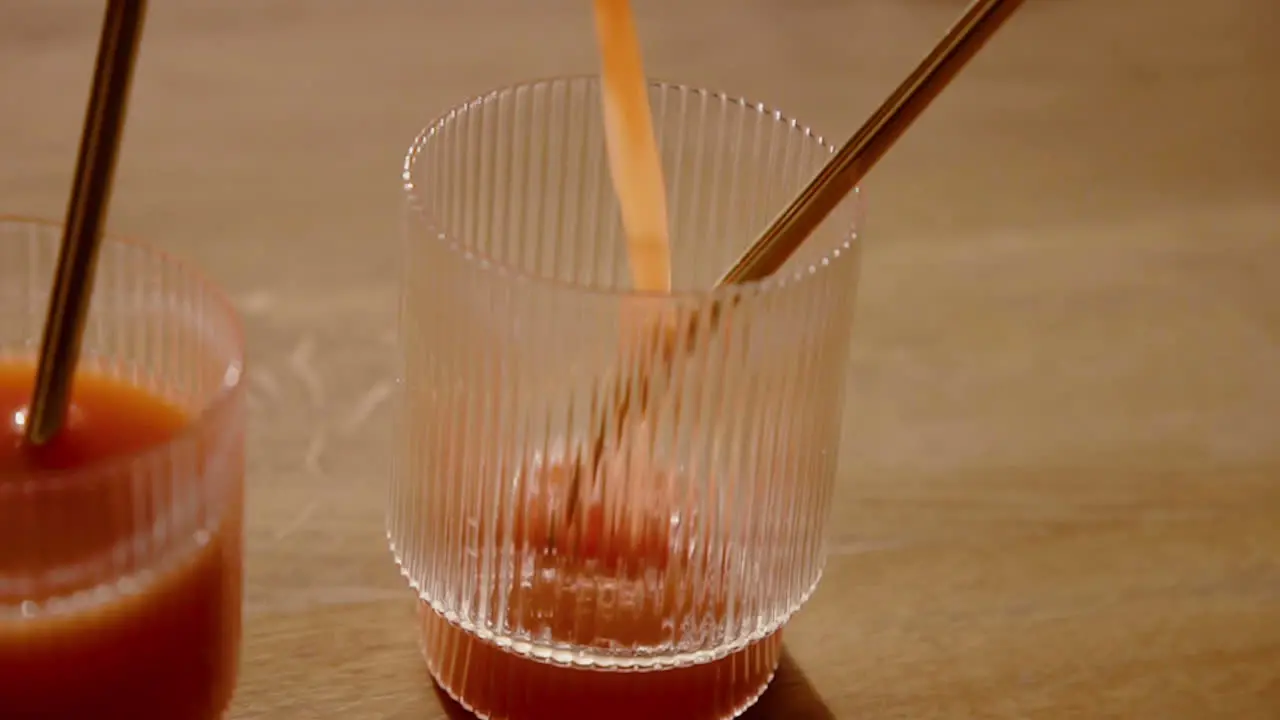 A Orange Cold Pressed Juice Detox Cleanse getting poured in a drinking glass with a metal straw in slow motion