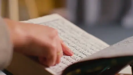 Close Up Of Person Turning Pages Of The Quran On Stand At Home